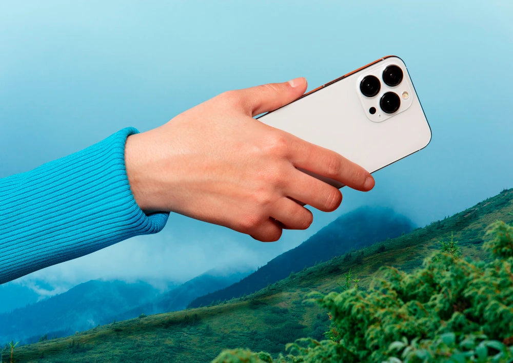 Hand houdt een refurbished iPhone vast boven een groen landschap met recyclingsymbool, CO2-besparing